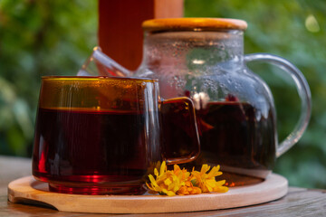Calendula flower healthy tea in glass mug with tea pot on garden table. Herbal medicine Delicious tisane tea with fresh yellow blossom dandelion flowers tea cup. Green clearing infusion Wildflowers