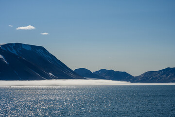 Peaceful early morning pastel blue landscape of mountain range, fog, sky, and Arctic ocean,...