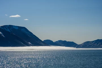 Fotobehang Peaceful early morning pastel blue landscape of mountain range, fog, sky, and Arctic ocean, Svalbard, as a polar nature background  © knelson20