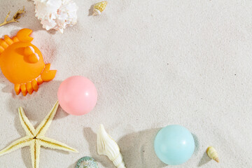 Colorful plastic balls, seashells and a silicone crab are decorated on a smooth sand background....