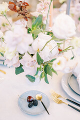 Berries on a saucer with a teaspoon stand on a set table next to a bouquet of flowers