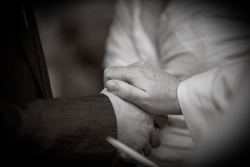 This emotive black and white photograph captures a close-up of two people holding hands in a...