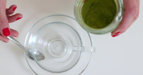 Woman is putting matcha powder in glass cup by the spoon