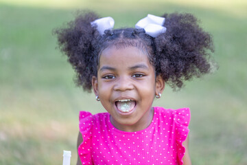 Happy preschooler African girl sticking his tongue out with candy, Kid girl playing outdoors in the...