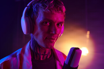 Portrait of smiling young man wearing headphones when singing in mike - obrazy, fototapety, plakaty
