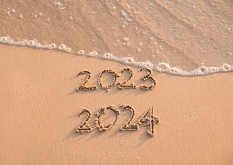Handwritten inscription 2023 and 2024 on the beach in the sunset time. The concept of Goodbye 2023 and Happy New Year 2024