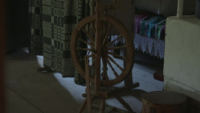 Tilt up shot of antique wooden spinning wheel in interior of authentic wooden hut. Old weaving equipment on legs in room at home, no people.
