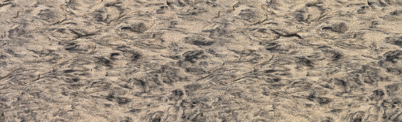 Abstraktes Muster aus schwarzem und braunem Sand in einem ebenen Boden am Strand bei Ebbe,...
