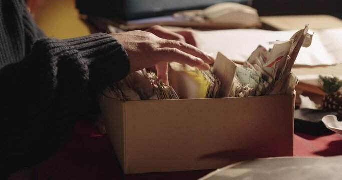 Person&rsquo;s hands rifling through a  cardboard box of old letters and trinkets. The background is a cluttered desk. Warm, nostalgic tone