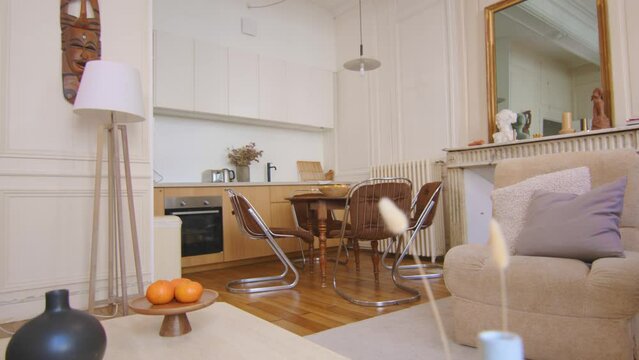Dolly shot off a modern kitchen and dining room. In the center of the frame there is a circular table and steel legs chairs In the background wooden kitchen. Other elements are lamps and small objects