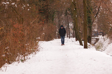 Man in black jacket walking in the snowy road among the trees