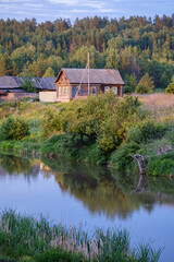 river in the foreground and an old Russian wooden village house on a summer evening in the sun