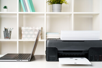 Modern printer with paper and laptop on table in office