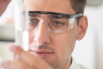 scientist male with lab glasses and gloves watching to green liquid