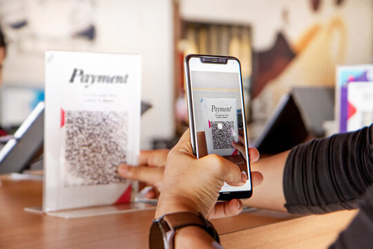 Customer using phone for payment at cafe restaurant, cashless QR code technology and money transfer concept