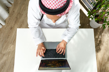 Young Arab man in traditional dress thobe working on computer in office