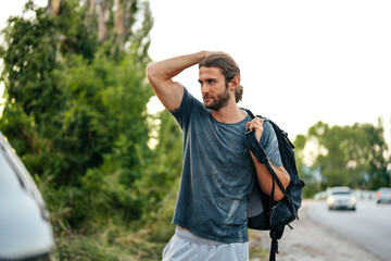 Portrait of young man hiker with backpack standing near his car