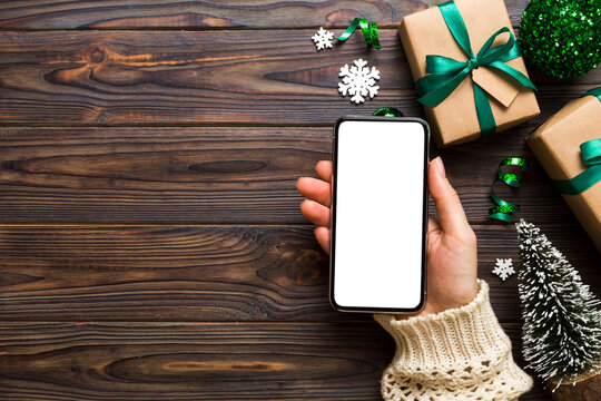 christmas mockup with space for text. christmas advertising, app template. hand holding phone with empty screen on table background. Happy New Year and Xmas Flat lay