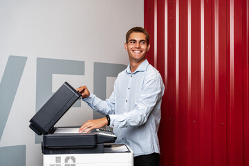 Positive young man using printer in the modern office