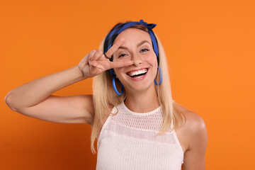 Portrait of smiling hippie woman showing peace sign on orange background
