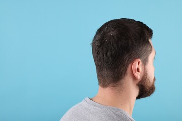 Man with dandruff in his dark hair on light blue background, space for text