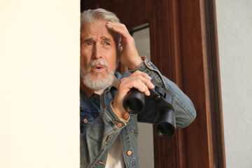 Concept of private life. Curious senior man with binoculars spying on neighbours outdoors