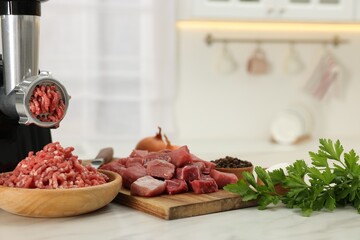 Electric meat grinder with beef and products on white marble table in kitchen