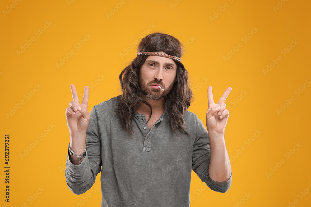 Wall mural Hippie man smoking cigarette and showing V-sign on orange background