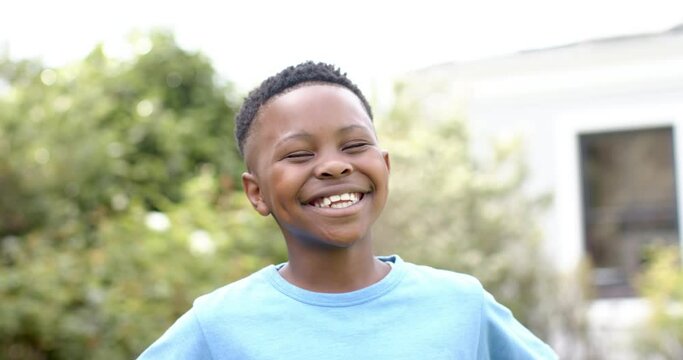 Portrait of happy african american boy laughing in sunny garden, slow motion