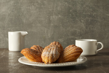 Madeleine cakes on plate, cup and milk jug on gray background