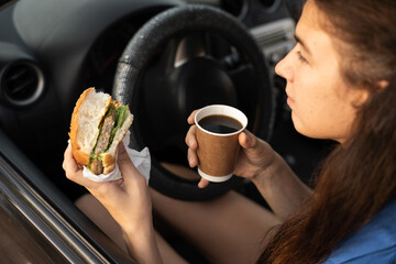 Business woman drinking coffee and eating hamburger in the car