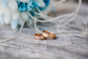 Engagement. Stylish rings, bouquet of white and blue flowers on a wooden background. Rings for the bride and groom. Vows. Luxury marriage and wedding accessory concept. Side view. Winter style.