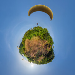 green grass little planet in blue sky with yellow paragliding parachute