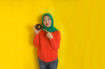 Beautiful muslim woman pointing to the donut with smiling while standing over yellow background