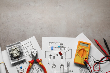 Wiring diagrams, digital multimeter and other electrician's equipment on grey table, top view. Space for text