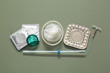 Contraceptive pills, condoms and intrauterine device on olive background, flat lay. Different birth control methods