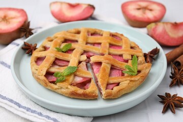 Delicious apple pie with mint and ingredients on white tiled table, closeup