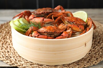 Delicious boiled crabs with lime and dill in bamboo steamer on table, closeup
