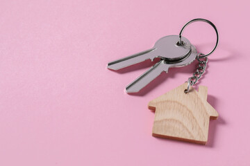 Metallic keys with wooden keychain in shape of house on pink background, space for text