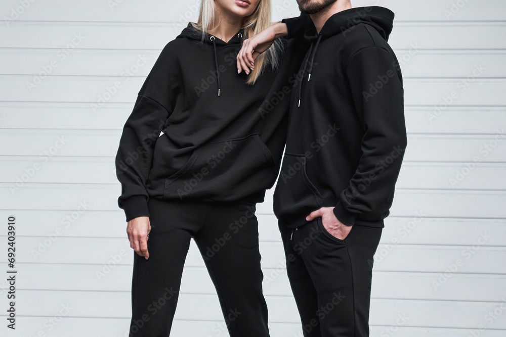 Wall mural Man and woman wear black hoodies.  A fashion template for print and branding on hoodie. trendy couple on the street wearing casual apparel with no face visible. No logo sweater and pullover with hood. - Wall murals