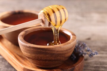 Pouring delicious honey from dipper into bowl on wooden table, closeup