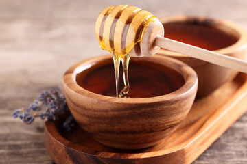 Pouring delicious honey from dipper into bowl on wooden table, closeup