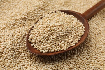 Wooden spoon and raw quinoa as background, closeup