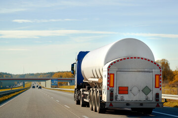 Dangerous goods transportation by semi truck with propane tank. The tank truck has a side view and shows hazard labels for high-temperature liquid and miscellaneous hazards. The truck follows the ADR - obrazy, fototapety, plakaty