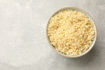 Delicious bulgur in bowl on light grey table, top view. Space for text