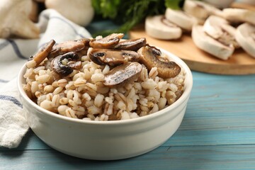 Delicious pearl barley with mushrooms in bowl on light blue wooden table, closeup