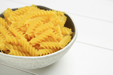 Raw fusilli pasta in bowl on white wooden table, closeup. Space for text