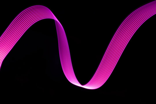 Pink and purple glow neon wave of light with smooth stripes on black background. Abstract background with flowing line in motion, light painting in vapor wave style.