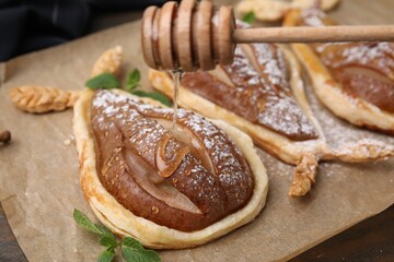 Pouring honey onto delicious pears baked in puff pastry with powdered sugar on table, closeup