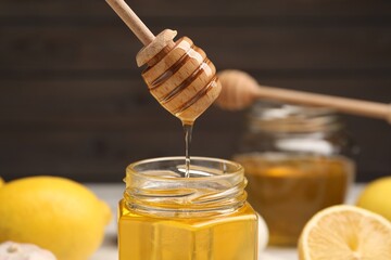 Honey dripping from dipper into jar against blurred background, closeup